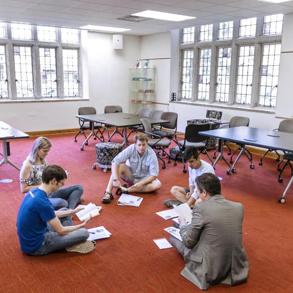一位教授和学生们围成一圈坐在红地毯上为即将到来的课程复习.